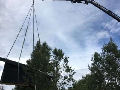 Shelter kranet på plads ind over grund omkranset af træer.